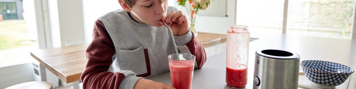 Kid drinks smoothie with blender on the table